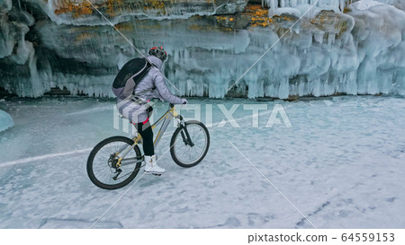 Woman is riding bicycle near the ice grotto. The rock with ice c 64559153