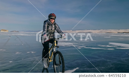 Woman is riding bicycle on the ice. Tires on bike are covered wi 64559210