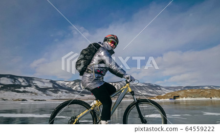 Woman is riding bicycle on the ice. Tires on bike are covered wi Woman is riding bicycle on the ice. Tires on bike are covered wi 64559222