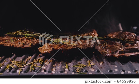 Delicious juicy meat steak cooking on grill. Prime beef fry on electric roaster, rosemary, black pepper, salt. Slow motion. Delicious juicy meat steak cooking on grill. Prime beef fry on electric roaster, rosemary, black pepper, salt. Slow motion. 64559956