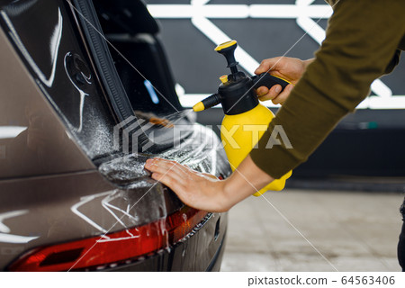 Worker wets rear bumper surface of car, detailing 64563406