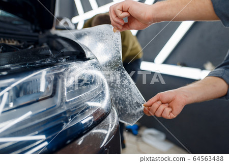 Worker applies car protection film on front fender Worker applies car protection film on front fender 64563488