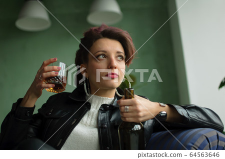Young sad woman with dark pink hair with glam rock style look is drinking whisky from a glass with abomination grimace on the face, female alcoholism, alcohol addiction Young sad woman with dark pink hair with glam rock style look is drinking whisky from a glass with abomination grimace on the face, female alcoholism, alcohol addiction 64563646