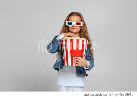 child girl wearing red-blue 3d glasses having fun and holding popcorn bucket child girl wearing red-blue 3d glasses having fun and holding popcorn bucket 64566643