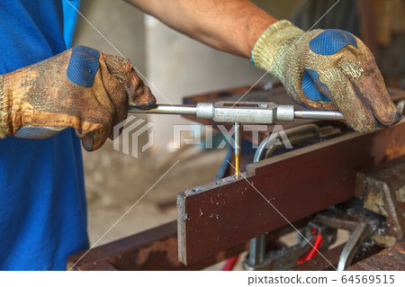 A man with protective gloves on his hands cuts a thread in metal for future connection A man with protective gloves on his hands cuts a thread in metal for future connection 64569515
