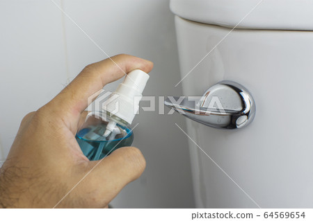 Alcohol sanitizer spray in hand is cleaning into toilet flush handle. Alcohol sanitizer spray in hand is cleaning into toilet flush handle. 64569654