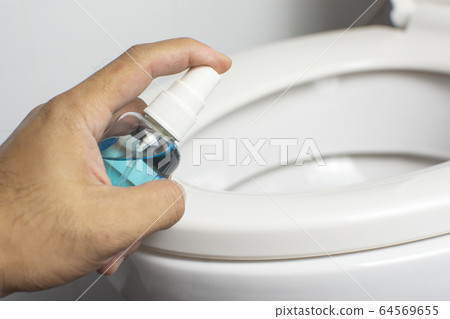 Alcohol sanitizer spray in hand is cleaning into toilet seat lid. Alcohol sanitizer spray in hand is cleaning into toilet seat lid. 64569655