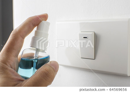 Alcohol sanitizer spray in hand is cleaning into lighting switch. Alcohol sanitizer spray in hand is cleaning into lighting switch. 64569656