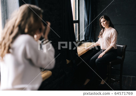 Woman model posing while sitting on chair in photo studio for unrecognizable female photographer Woman model posing while sitting on chair in photo studio for unrecognizable female photographer 64571769