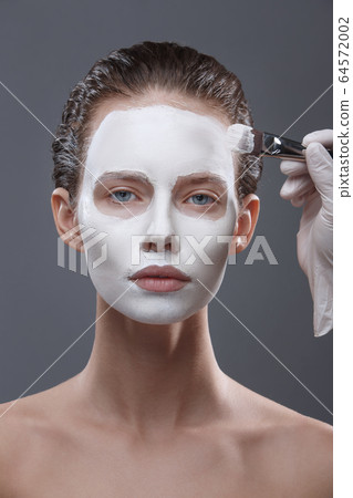 Beautiful girl is applied a white cosmetic mask from black dots. Isolate, studio 64572002
