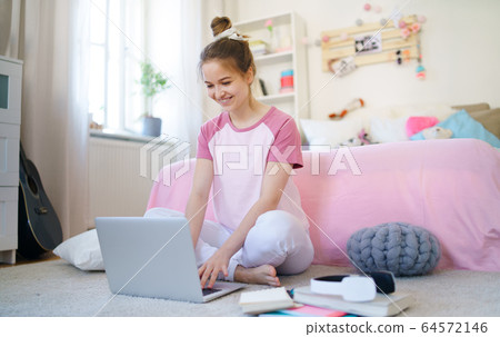 Young girl with laptop sitting on floor, relaxing during quarantine. 64572146