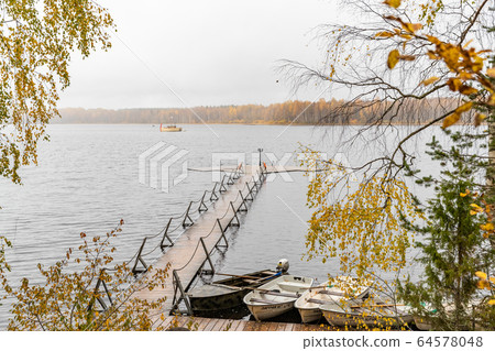 The Long pier on the lake, Terrace at the lake, the Autumn at the lake Boroye, Boats at a pier, Valday national park, Russia, panoramic image, golden trees, Wooden lodges, cloudy weather 64578048