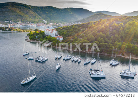 Aerial view of marina Vis at sunset, Croatia, a lot of chaotically standing boats in a bay, roofs of orange color, sunshine, hills with green trees, ferry station 64578218