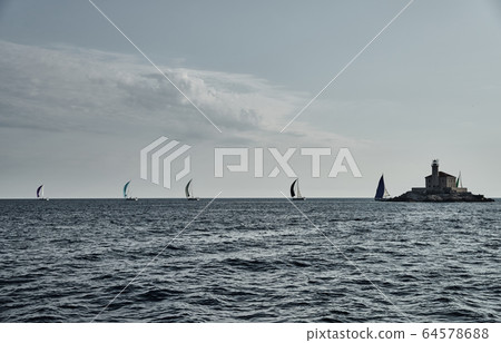 Sailboats compete in a sail regatta at sunset, Boats bend around the island with a beacon, a race, multicolored spinnakers, number of boat is on aft boats, island is on background, clear weather Sailboats compete in a sail regatta at sunset, Boats bend around the island with a beacon, a race, multicolored spinnakers, number of boat is on aft boats, island is on background, clear weather 64578688