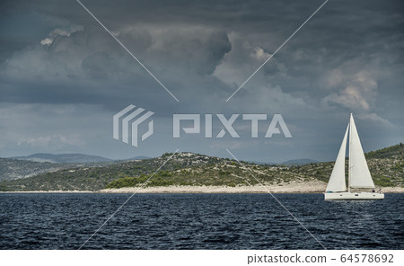 Sailboat of white color, reflection of sail is on water, clouds, the island is on background, sunny weather Sailboat of white color, reflection of sail is on water, clouds, the island is on background, sunny weather 64578692