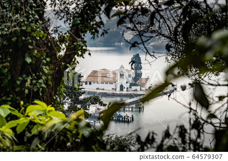 Monastery Vlacherna and the Mouse Island at clouds rainy weather through branches of trees, sea gulf, the airport runway is nearby, Kanoni, Corfu, Greece 64579307