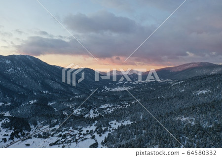 The Aerial view of a sunset over mountain in Arahova, Greece, a view of the valley below with trees covered by snow, colors of sunset 64580332