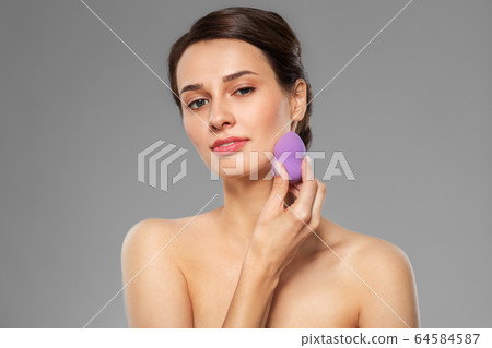 young woman with sponge applying makeup 64584587