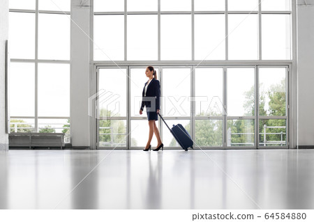 businesswoman with travel bag walking along office businesswoman with travel bag walking along office 64584880
