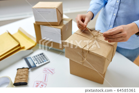woman packing parcel and tying rope at post office woman packing parcel and tying rope at post office 64585361