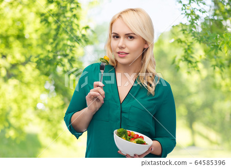 smiling young woman eating vegetable salad 64585396