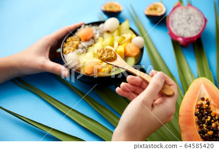 hands with mix of exotic fruits and wooden spoon 64585420