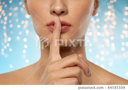 beautiful young woman holding finger on lips 64585509