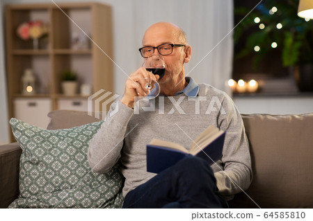 senior man with book drinking red wine at home 64585810