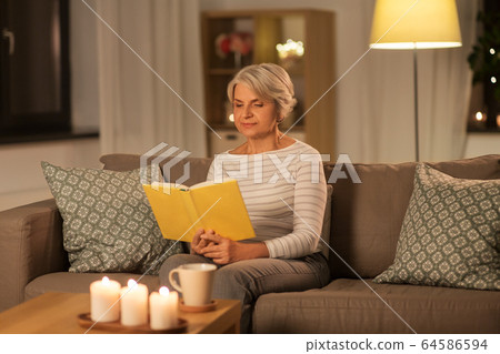 happy senior woman reading book at home in evening happy senior woman reading book at home in evening 64586594
