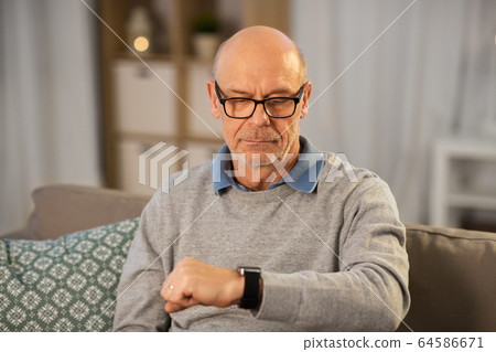 senior man looking at wristwatch at home 64586671