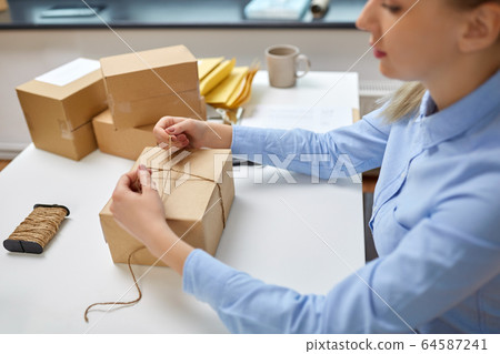 woman packing parcel and tying rope at post office woman packing parcel and tying rope at post office 64587241