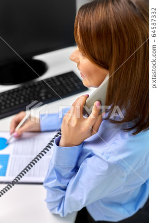 businesswoman calling on desk phone at office businesswoman calling on desk phone at office 64587332