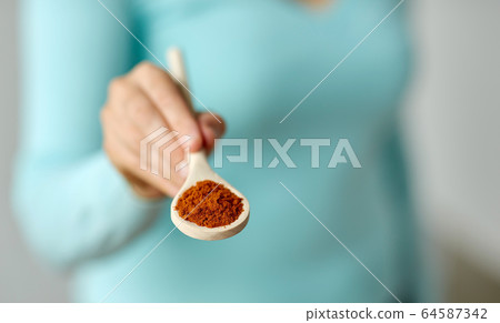 close up of woman with turmeric on wooden spoon 64587342