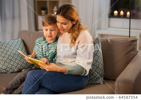 happy mother and son reading book sofa at home 64587354