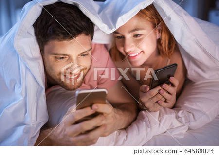 happy couple using smartphones in bed at night happy couple using smartphones in bed at night 64588023
