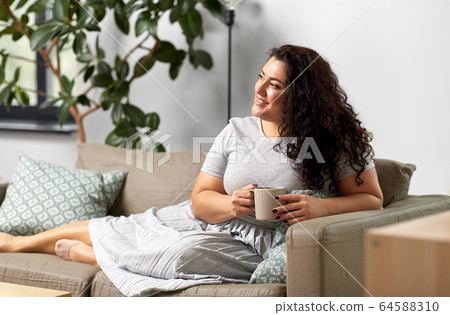 happy woman drinking coffee or tea on sofa at home happy woman drinking coffee or tea on sofa at home 64588310