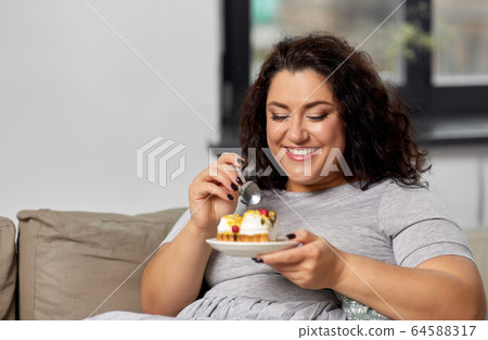 smiling young woman eating cake at home smiling young woman eating cake at home 64588317