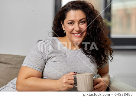 happy woman drinking coffee or tea on sofa at home happy woman drinking coffee or tea on sofa at home 64588493