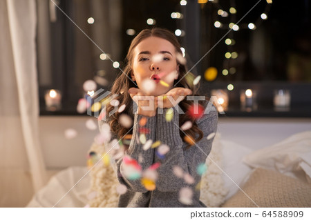 woman blowing confetti from her hands at home 64588909