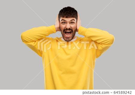 man in yellow sweatshirt closing ears by hands man in yellow sweatshirt closing ears by hands 64589242