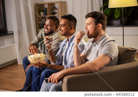 male friends with popcorn watching tv at home male friends with popcorn watching tv at home 64589312