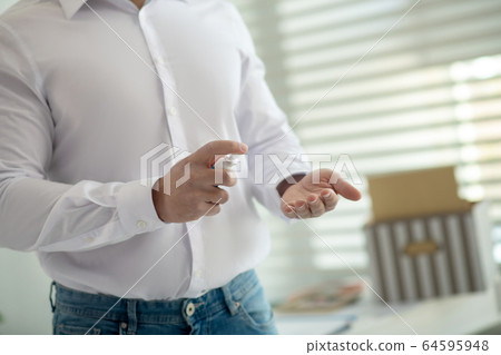 Dark-haired man in a protective mask spraying sanitizer on his hands 64595948