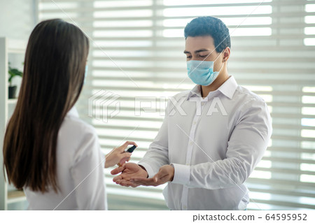 Long-haired girl spraying sanitizer on her colleagues hands 64595952