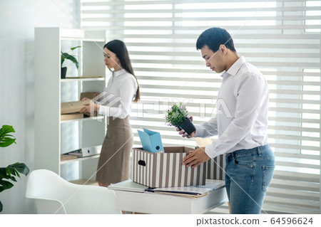 Upset young brunette male personal stuff into box 64596624