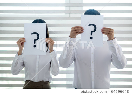 Male and female colleagues standing at the window, covering thier faces with papers with question marks 64596648