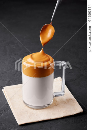 Dalgona Coffee in a transparent cup at black slate. Dalgona Frothy Coffee is a popular Korean drink Dalgona Coffee in a transparent cup at black slate. Dalgona Frothy Coffee is a popular Korean drink 64600554