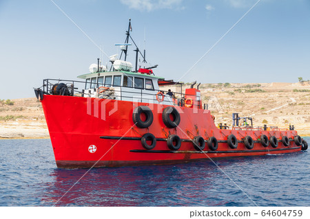 Tug boat with bright red hull goes near  Malta 64604759