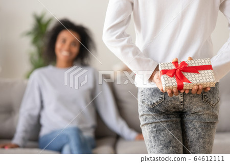 Rear view of teen african daughter holding gift behind back 64612111