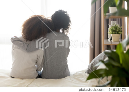 Loving african single mother embrace teen daughter sit on bed Loving african single mother embrace teen daughter sit on bed 64612473