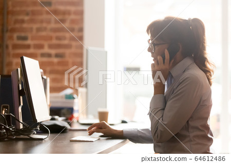 Serious businesswoman talking on phone using computer in office Serious businesswoman talking on phone using computer in office 64612486